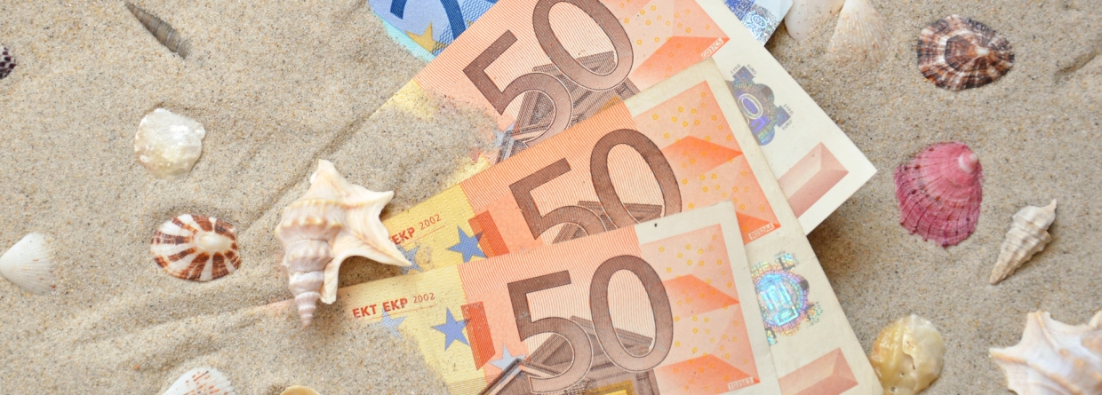 Meerdere briefjes geld op een strand met schelpen