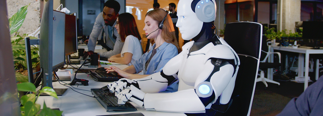 In een ebdrijf zit een robot achter de computer naast mensen