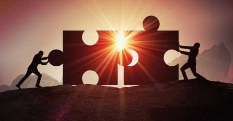 twee mannen duwen een puzzelstuk naar elkaar toe met zon opkomst op de achtergrond