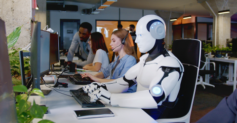In een ebdrijf zit een robot achter de computer naast mensen